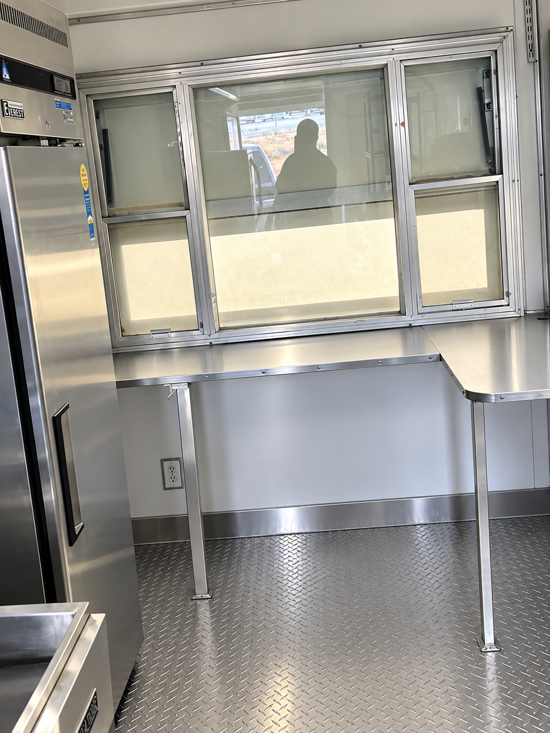 Stainless steel service counter and pass-through window inside a commercial mobile kitchen